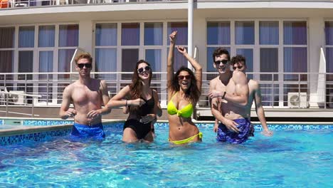 Happy-young-cheerful-friends-dancing-and-having-fun-in-the-pool-cooling-off-in-the-water-on-a-hot-summer-day.-Summertime-pool-party.-Slowmotion-shot.