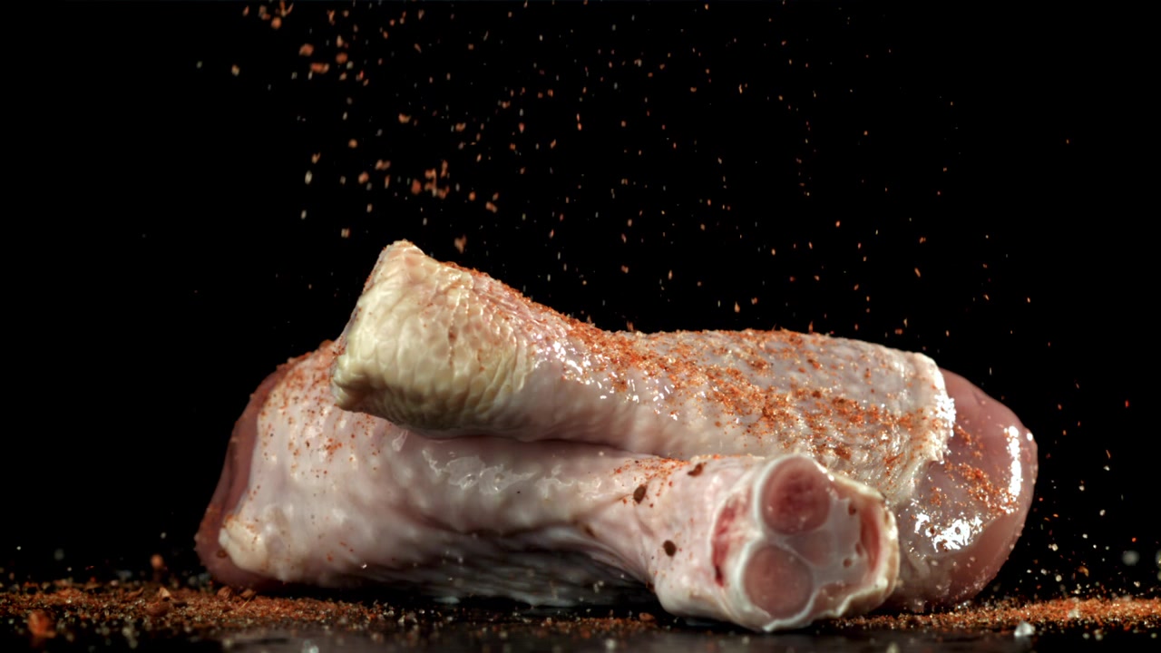Spezie che cadono su cosce di pollo crude al rallentatore