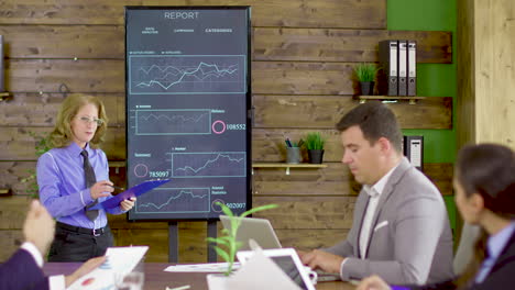 female in a conference room pointing at statistics on tv screen