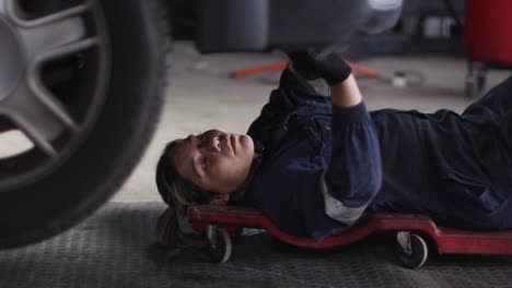 female mechanic lying and working under car at a car service station