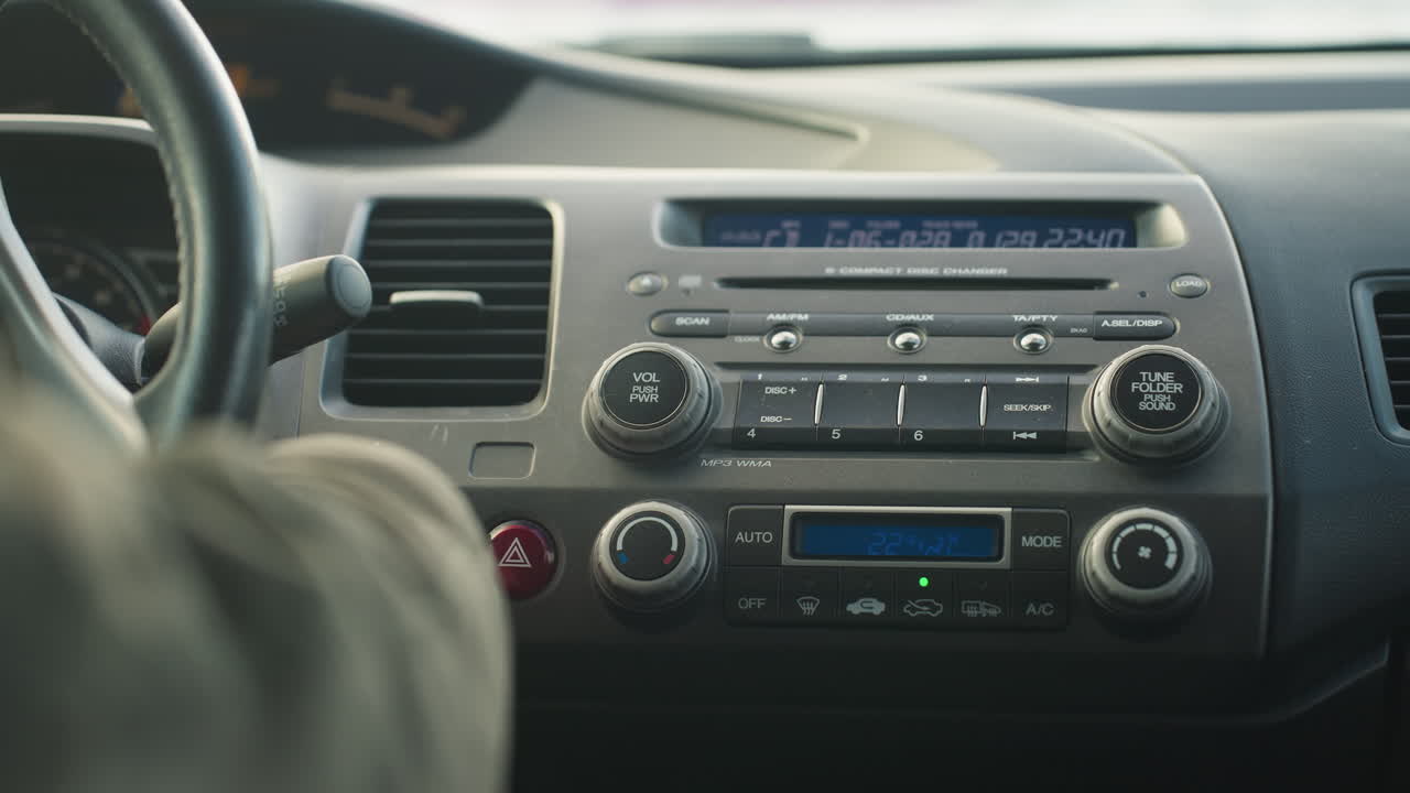 rear view of driver starting car with dashboard panel lighting up, finger near ignition, central console display and buttons active, with hand and steering wheel partially visible