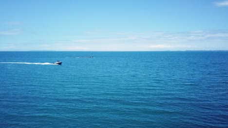 Luftaufnahme-Einer-Drohne,-Die-Einem-Schnellboot-Von-Der-Seite-Eines-Entfernten-Bootes-Folgt,-Das-Eine-Lange-Bootsspur-Mitten-Im-Meer-Erzeugt