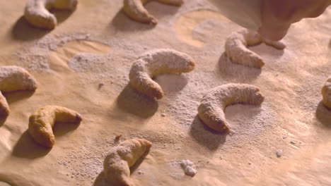 sprinkling powdered sugar over crescent shaped cookies on baking sheet. close up
