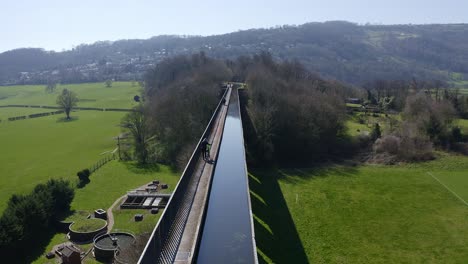 Un-Ciclista-Que-Camina-Por-La-Hermosa-Ruta-Estrecha-Del-Canal-De-Botes-Llamada-El-Acueducto-Pontcysyllte,-Famoso-Diseñado-Por-Thomas-Telford,-Ubicado-En-La-Hermosa-Campiña-Galesa,-Puente