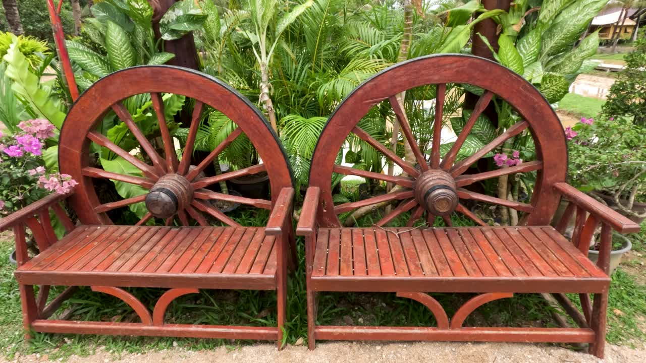 Handcrafted wooden bench with wagon wheel arms in lush tropical garden, natural daylight, static shot