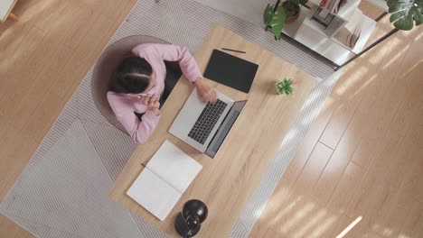 vista superior zoom shot de una mujer hablando en el teléfono inteligente mientras está sentado en el escritorio de madera escribiendo en una computadora portátil en casa