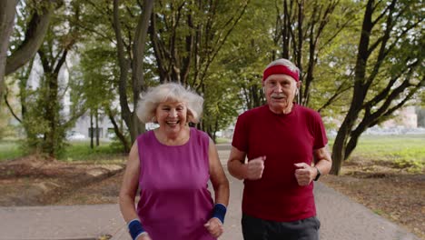 active senior elderly couple doing cardio morning exercise workout. man, woman running in city park.