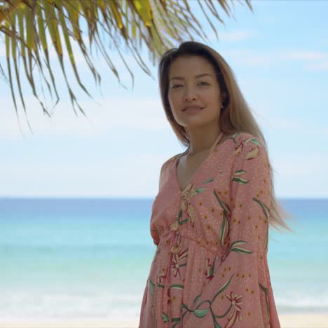 Cheerful-female-standing-near-palm-on-beach