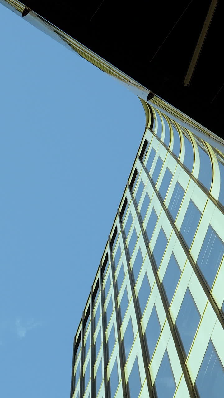 Una sorprendente inquadratura verticale dal basso di un moderno grattacielo aziendale con finestre in vetro riflettente contro un cielo azzurro limpido. Perfetto per contenuti aziendali e di sviluppo urbano.