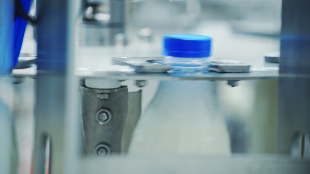 Robotic machine of twisting lid on a plastic bottle. Automated process of putting cover on a bottle with milk in a modernized diary plant. Close-up.
