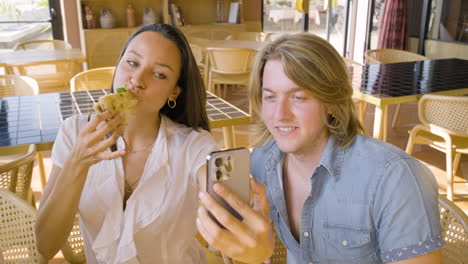 niña feliz comiendo pizza y tomando una foto selfie con su amigo en un restaurante 1