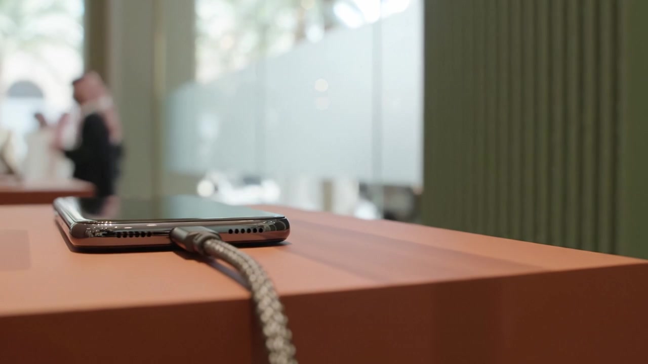 Primo piano di uno smartphone appoggiato su una superficie elegante e moderna con un cavo di ricarica collegato, che mostra una fusione di tecnologia e design contemporaneo.