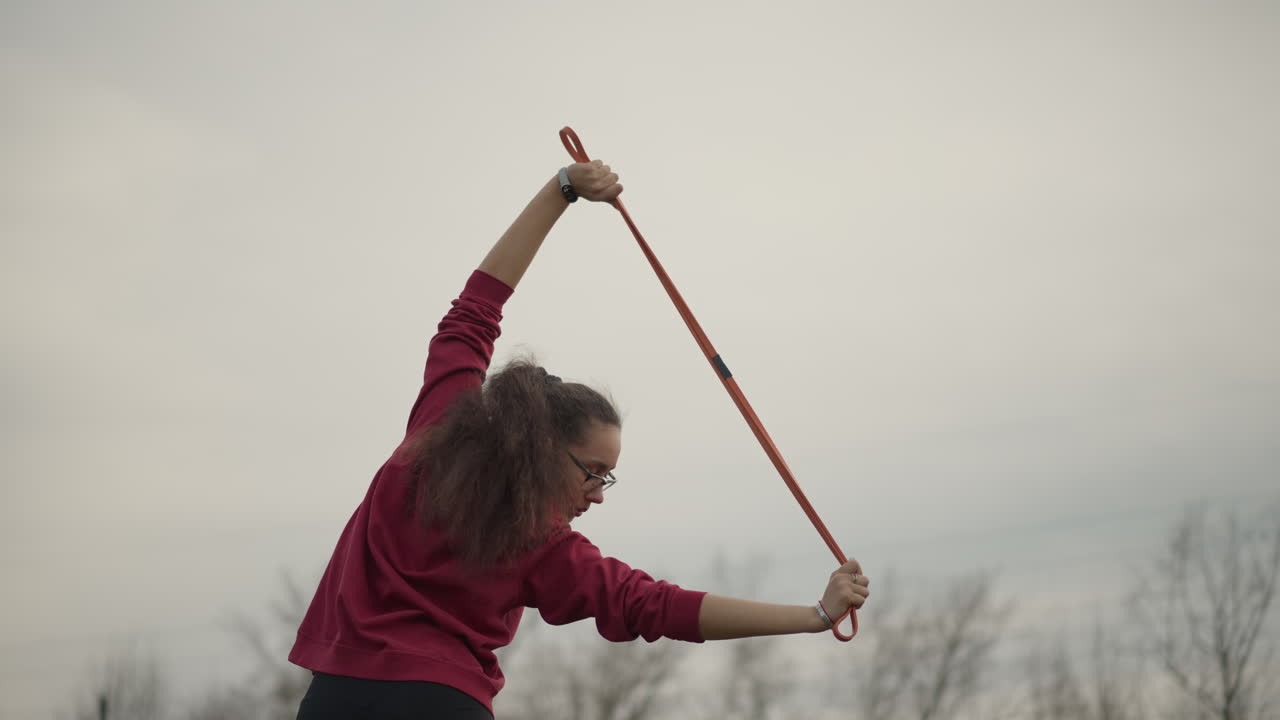 Caucasian Woman Stretching Ribbon Toward Horizon. Dramatic Skyline Backdrop With Power Lines, Wide Open Field, BackFacing Stance, Controlled Motion And Contemplative Training Mood