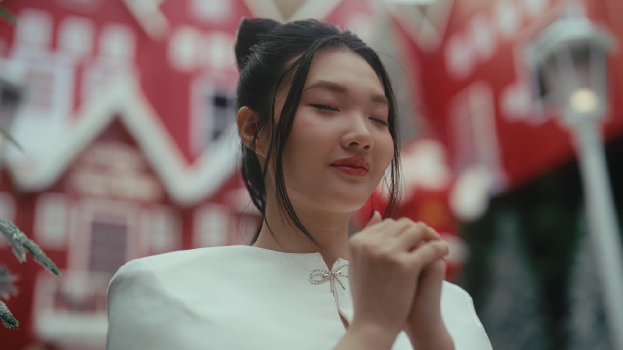A woman prays peacefully outdoors near festive red buildings, serene and hopeful