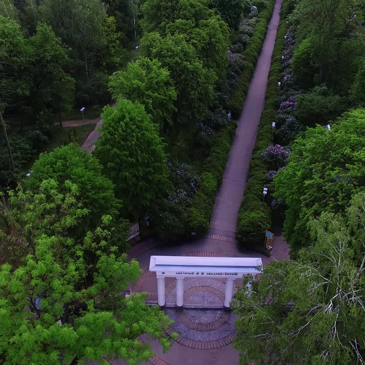 Charming white entrance with columns to a green park. Drone rising over the beautiful territory of historical country seat with museum