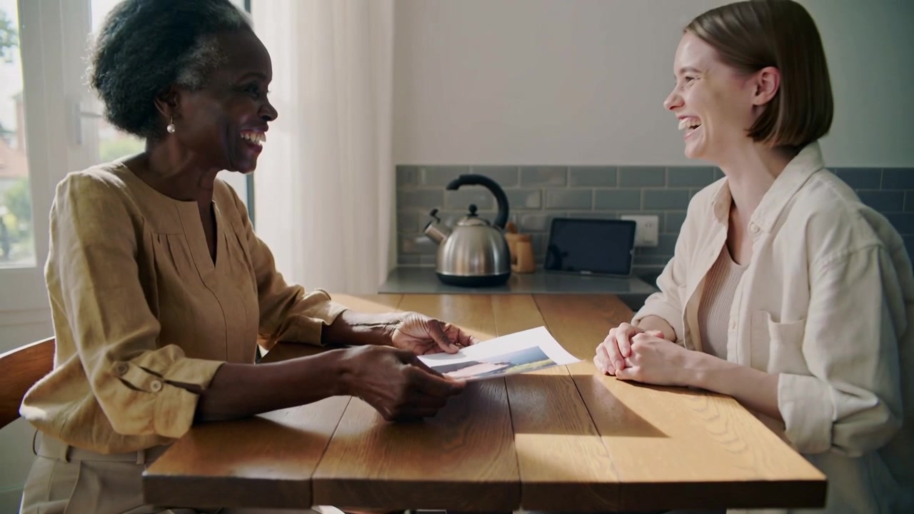 Placing senior in blouse showing print at kitchen table, sharing with adult light shirt laughing