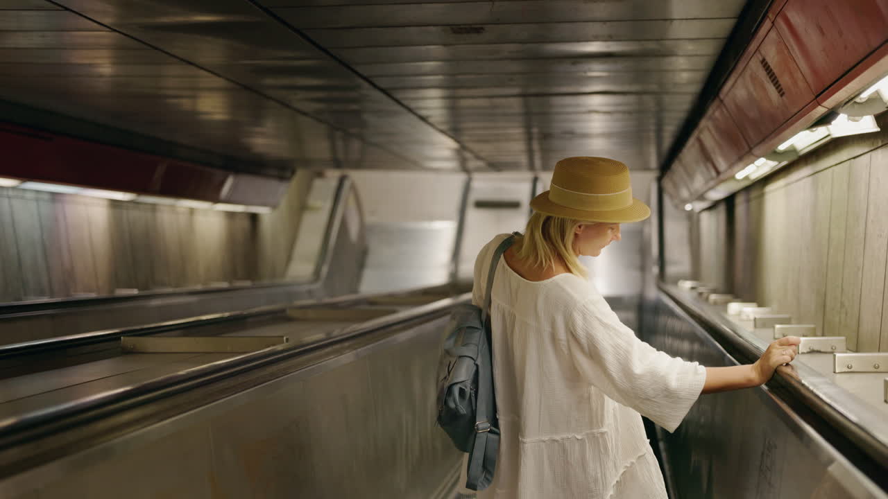 Woman with backpack and hat riding an escalator in a subway tunnel