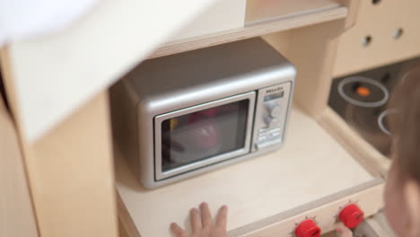 niña de 3 años jugando en la cocina de juguete - usando el microondas de los niños, gire la perilla del horno - cámara lenta de primer plano