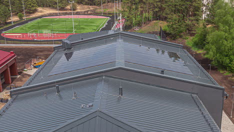 New-school-construction-with-solar-panels-installed-over-the-gymnasium-sports-center---time-lapse-of-sunshine,-shadow-and-workers-on-the-roof