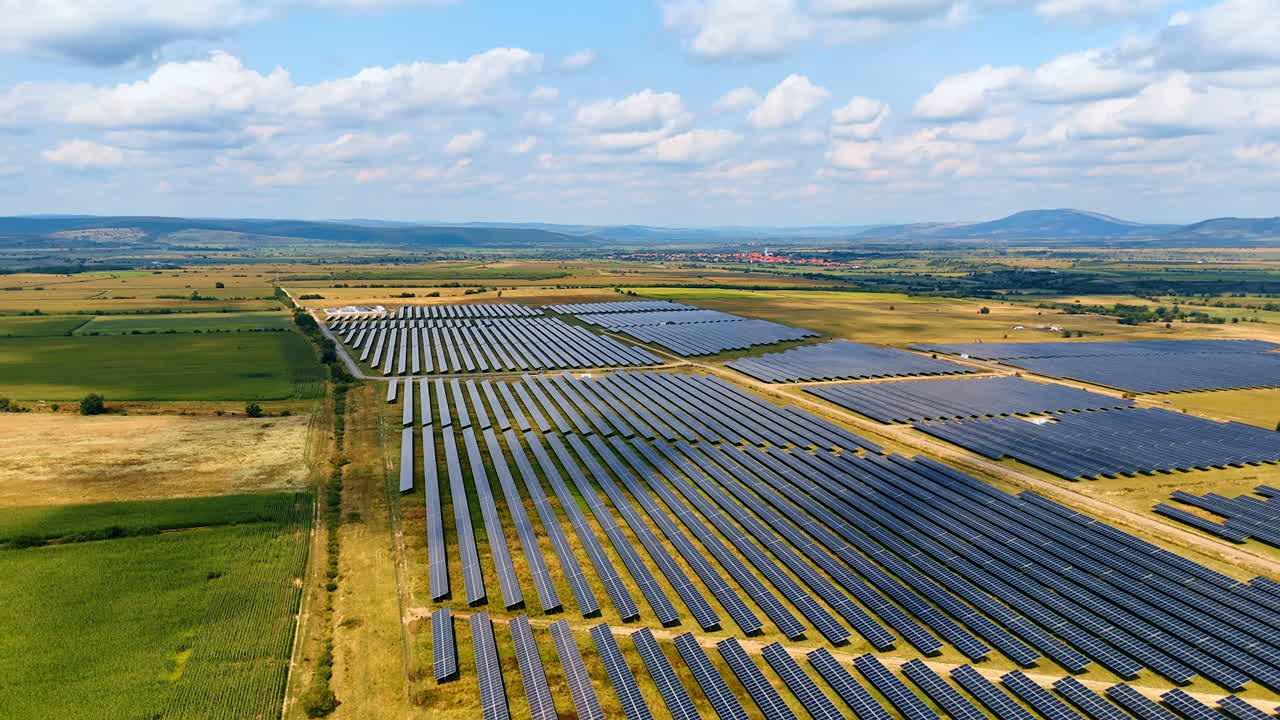 Solcellepark omgivet af landbrugsjord. Dronefoto af en stor solcellepark omgivet af landbrugsmarker under en blå himmel
