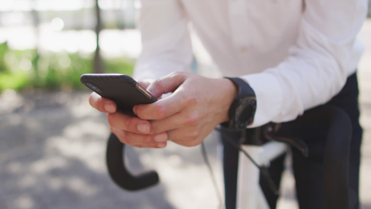 sección media del hombre usando un teléfono inteligente mientras se apoya en su bicicleta en la calle