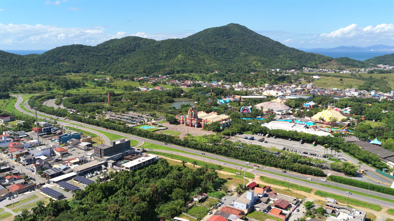 Beto Carrero World theme park in Penha, surrounded by lush tropical vegetation and green hills. Forward aerial approach on clear tropical day.