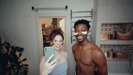 joven pareja multiétnica con parches debajo de los ojos tomando selfies en el baño