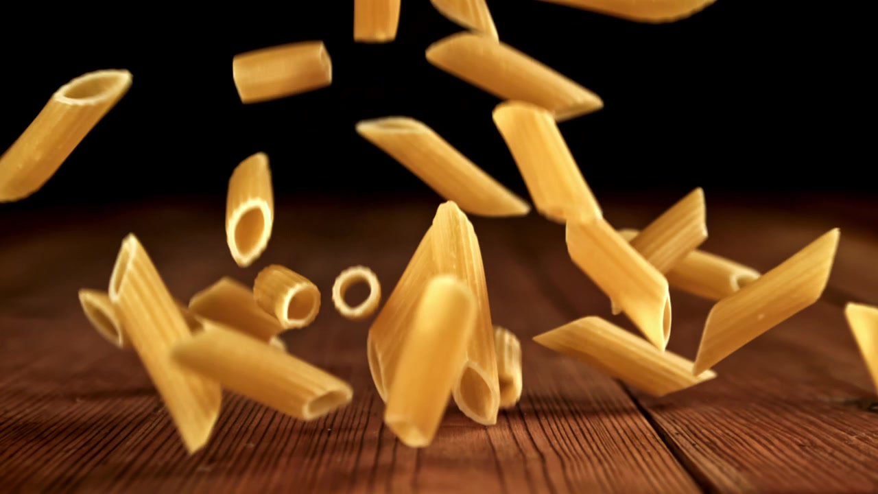 Pasta Penne che cade su un tavolo di legno al rallentatore