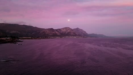 Full-moon-rises-over-the-mountains-and-ocean-at-twilight