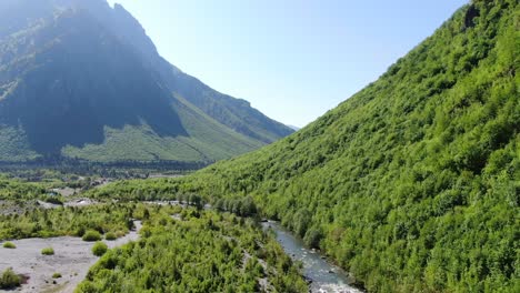 Vista-De-Drones-En-Albania-En-Los-Alpes-Volando-Sobre-Un-Río-Rodeado-De-Montañas-Verdes-Llenas-De-árboles-A-Los-Lados-En-El