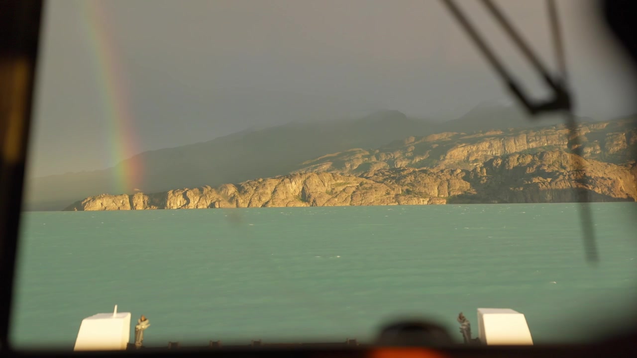 Rainbow above Lago Argentino near El Calafate, Santa Cruz, Patagonia, Argentina, with turquoise glacial waters, eroded sedimentary cliffs and Andes foothills viewed from moving boat, slow motion POV