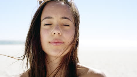 close up portrait of beautiful young woman running hand through hair blowing in wind  on tropical beach slow motion