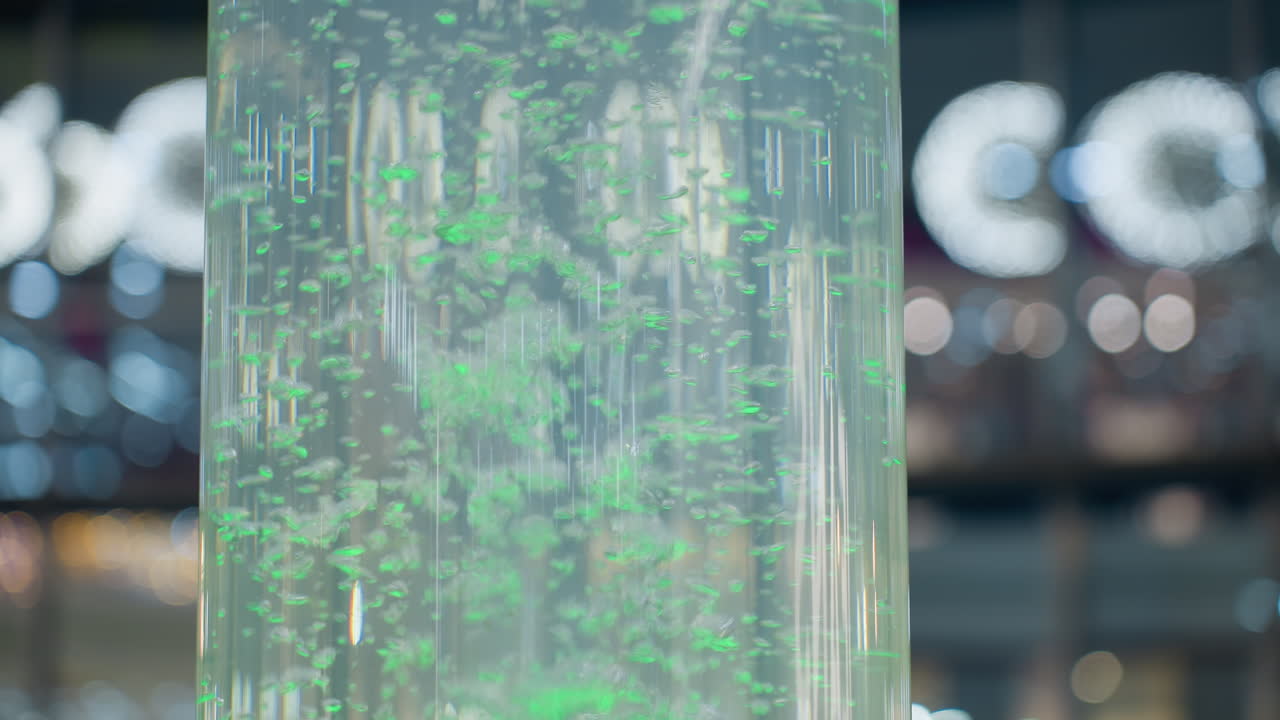 Close-up of large cylindrical water feature with green and blue glowing water bubbles, soft bokeh light effect in the background creates a calming and festive atmosphere