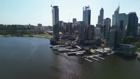 aerial approaching shot of perth skyline with port at swan river during sunny day - construction site with working cranes on tower in city