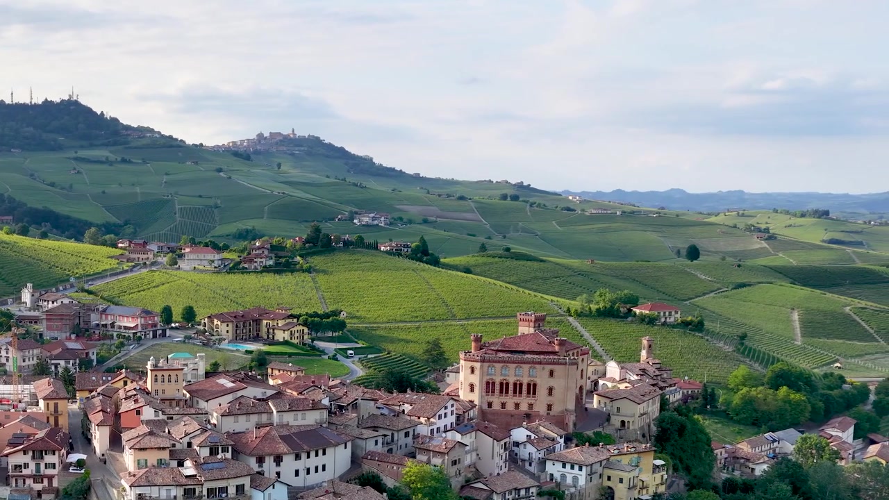 Ampia ripresa aerea con drone di uno storico borgo italiano circondato da dolci colline verdi di vigneti.