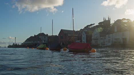 sail boats floating in fowey harbour beside waterfront homes in evening sunshine, cornwall, england - low angle