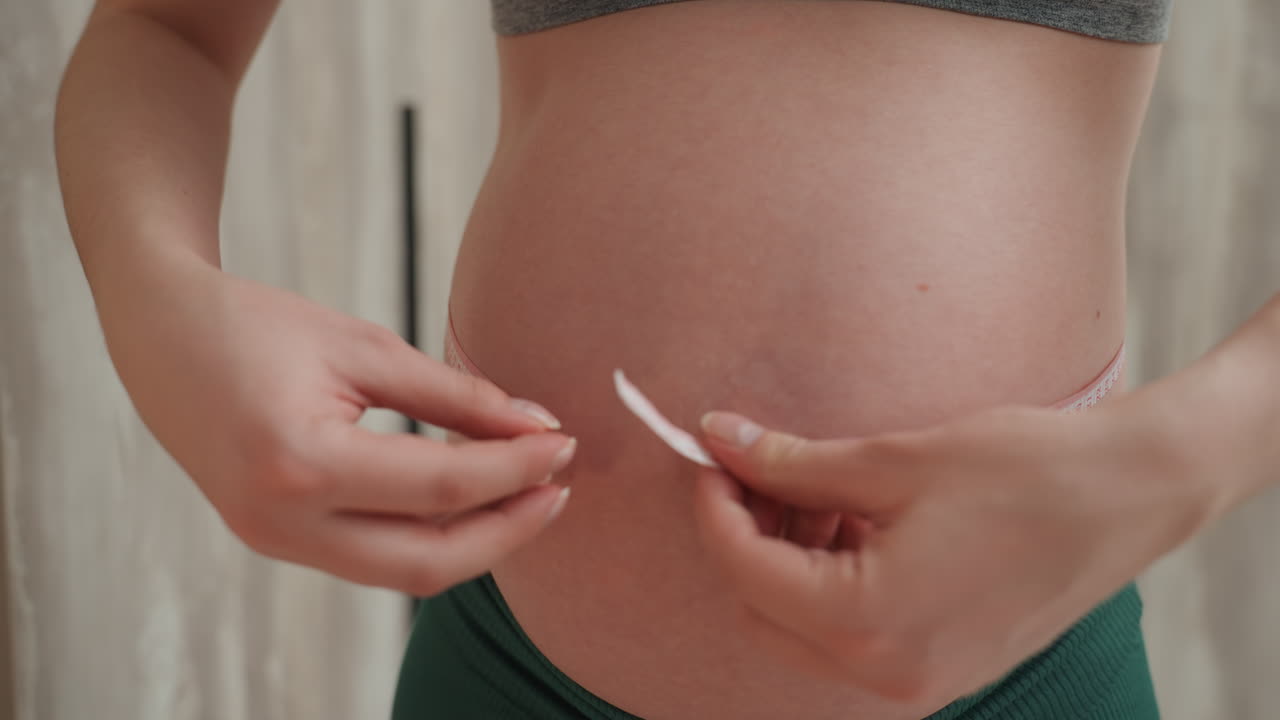 Donna incinta che misura la pancia in primo piano con un metro a nastro morbido, mani concentrate che segnano la circonferenza e monitorano la crescita, texture della pelle dettagliata e rituale di misurazione per il monitoraggio e la pianificazione prenatale.