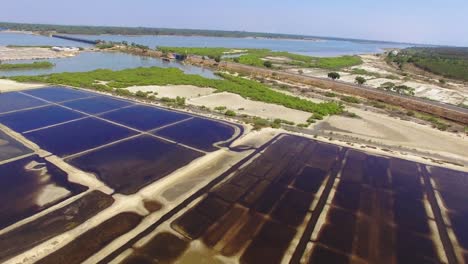 Drone-footage-moving-forwards-and-downwards-across-a-salt-pan-with-the-East-coast-road,-India-in-the-background