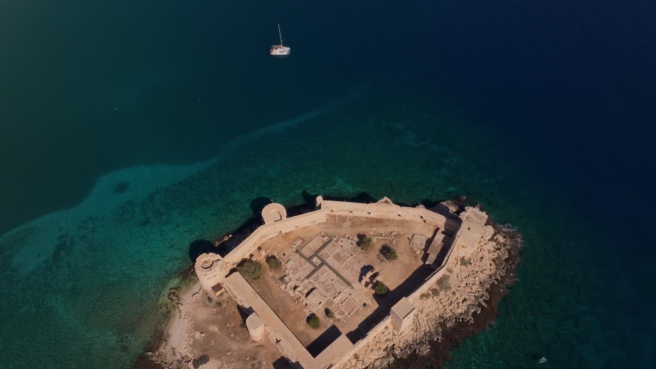 Castello medievale arroccato sopra il calmo Mediterraneo con uno yacht nelle vicinanze