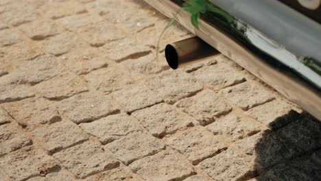 un primer plano de la tubería de escape de un coche clásico y un detalle cromado sobre el pavimento de adoquines
