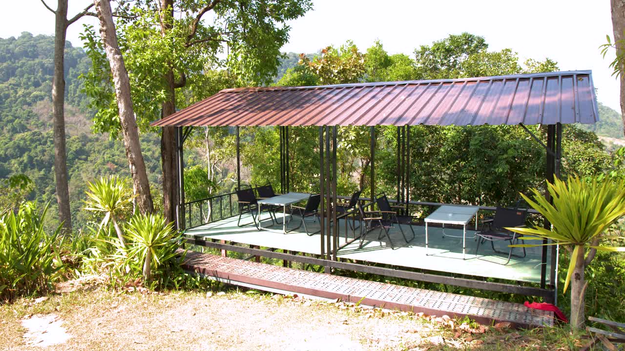 Wide shot of a metal roof terrace with folding chairs overlooking a tropical forest