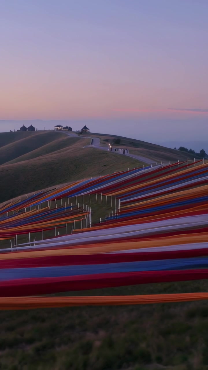 Vidéo verticale : Caméra panoramique vers la droite montrant de larges bandes de tissu traversant une colline verdoyante au crépuscule avec des poteaux