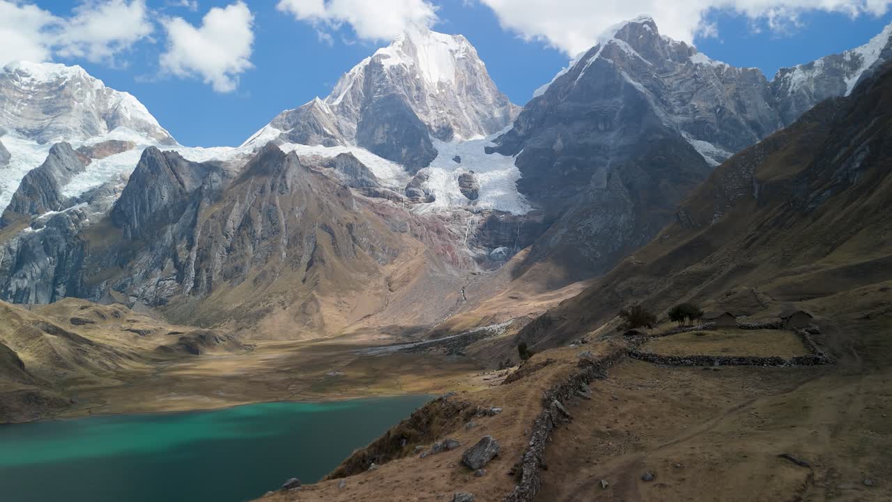 Una maestosa ripresa aerea rivela lo splendido paesaggio del trekking di Huayhuash in Perù, mostrando laghi glaciali turchesi, antiche rovine e montagne andine innevate.