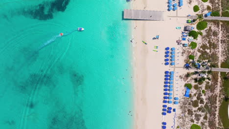 Stunning-aerial-view-of-Grace-Bay-Beach-in-Providenciales,-featuring-a-tubing-boat,-beach-pier,-white-sand,-and-turquoise-waters