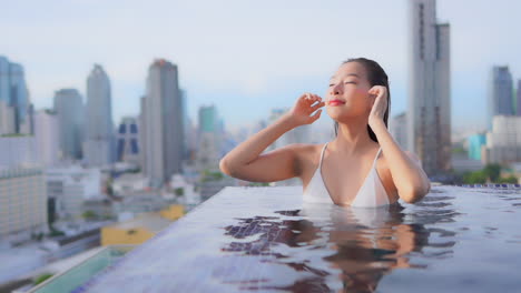 ภูเขารามเมืองกรอบหญิงสาวที่น่าดึงดูดที่ขอบของสระว่ายน้ําอินฟินิตี้ล้างผมเปียกของเธอกลับจากใบหน้าของเธอ, แบงค็อก, ประเทศไทย
