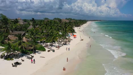 Paisaje-Aéreo-De-Turistas-Caminando-En-Una-Hermosa-Playa-De-Arena-Blanca-Con-Costa-Azul-Turquesa-En-Tulum-México