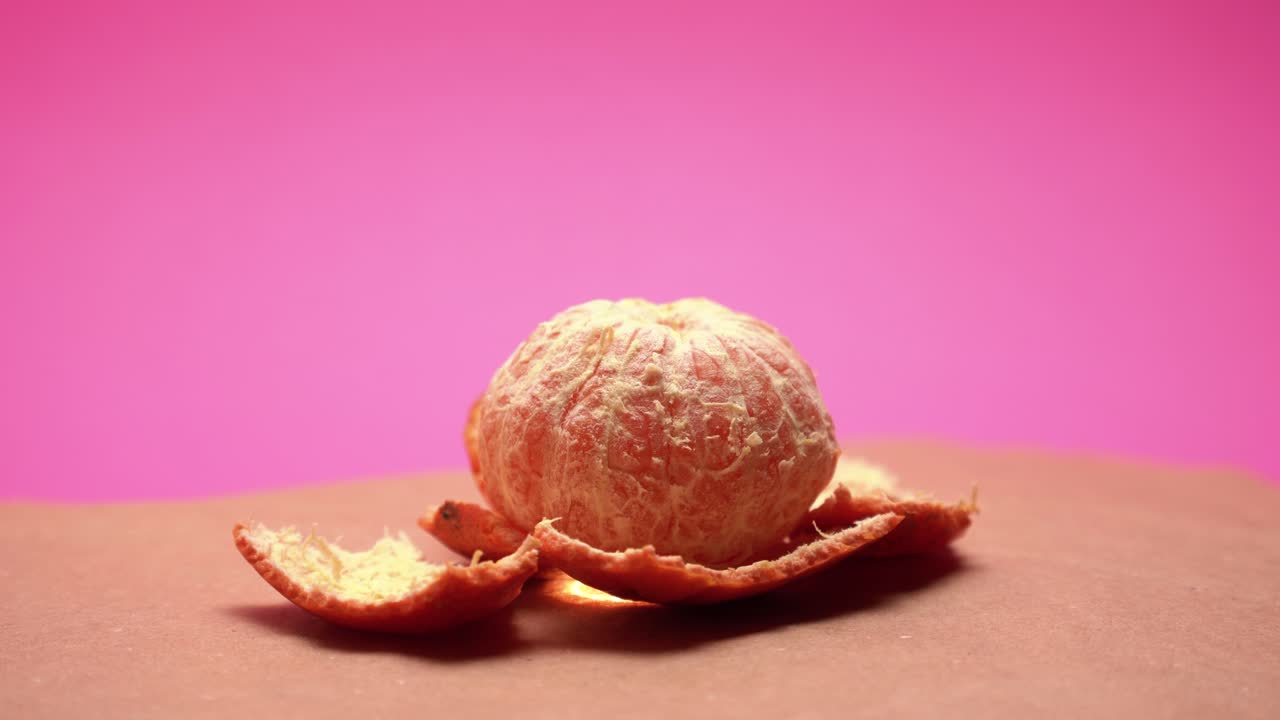 mandarina madura pelada, gire en video de 4k de fondo de papel rosa y viejo con corrección de color