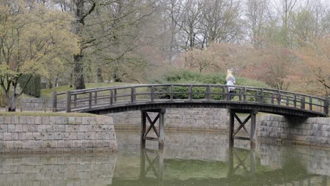 Chica-Con-Traje-De-Anime-Cosplay-Cruzando-El-Puente-De-Madera-En-El-Jardín-Japonés-En-Hasselt,-Bélgica