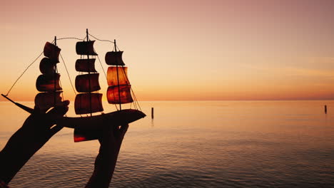 Mann-Hält-Ein-Spielzeugsegelboot-Vor-Dem-Hintergrund-Des-Seereise--Und-Entdeckungskonzepts