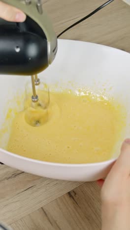 vertical close-up of egg yolk and powdered sugar being mixed to create a creamy tiramisu base.